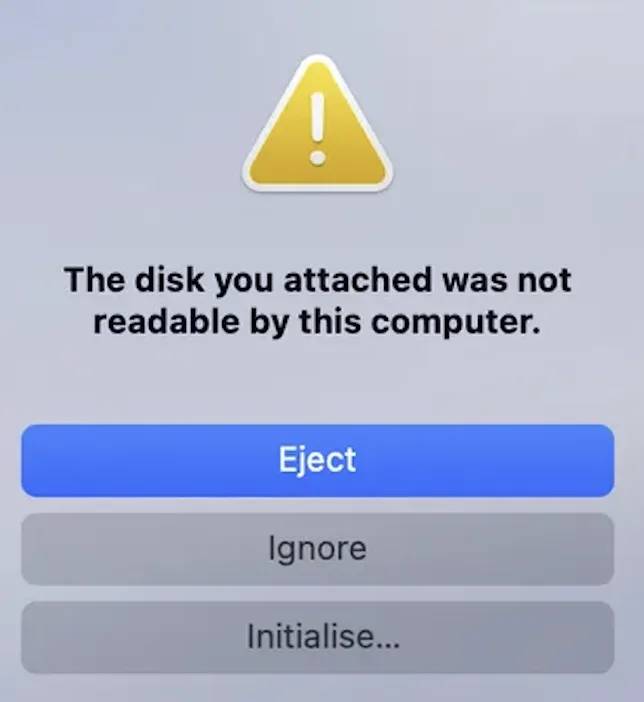 The macOS alert shown without LuksMac: &ldquo;The disk you attached was not readable by this computer,&rdquo; offering only Eject, Ignore and Initialise.